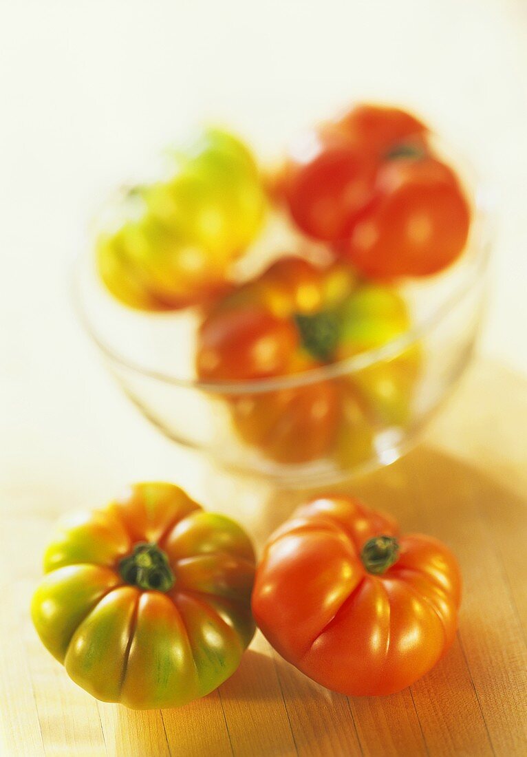 Beefsteak tomatoes, ripe & unripe, in front of & in glass bowl