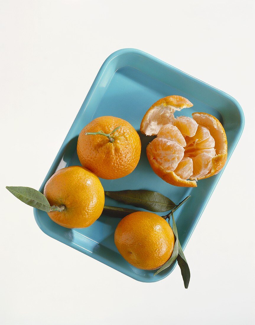 Three whole mandarins and one peeled one on small tray