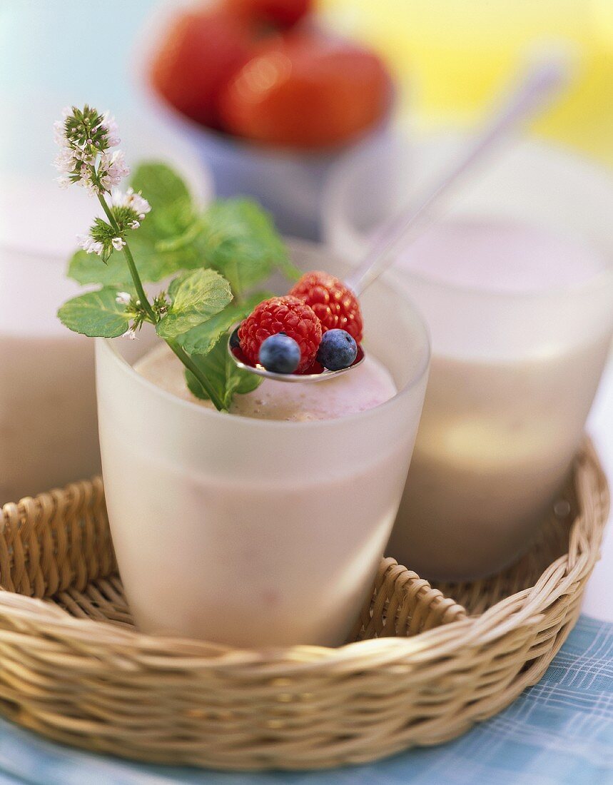 Beerenmilch in Bechern auf Tablett, darüber Löffel mit Beeren