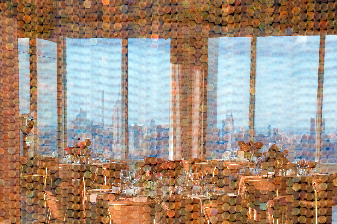 View through a hexagonal patterned curtain of a restaurant dining area with cityscape featuring Empire State building in background