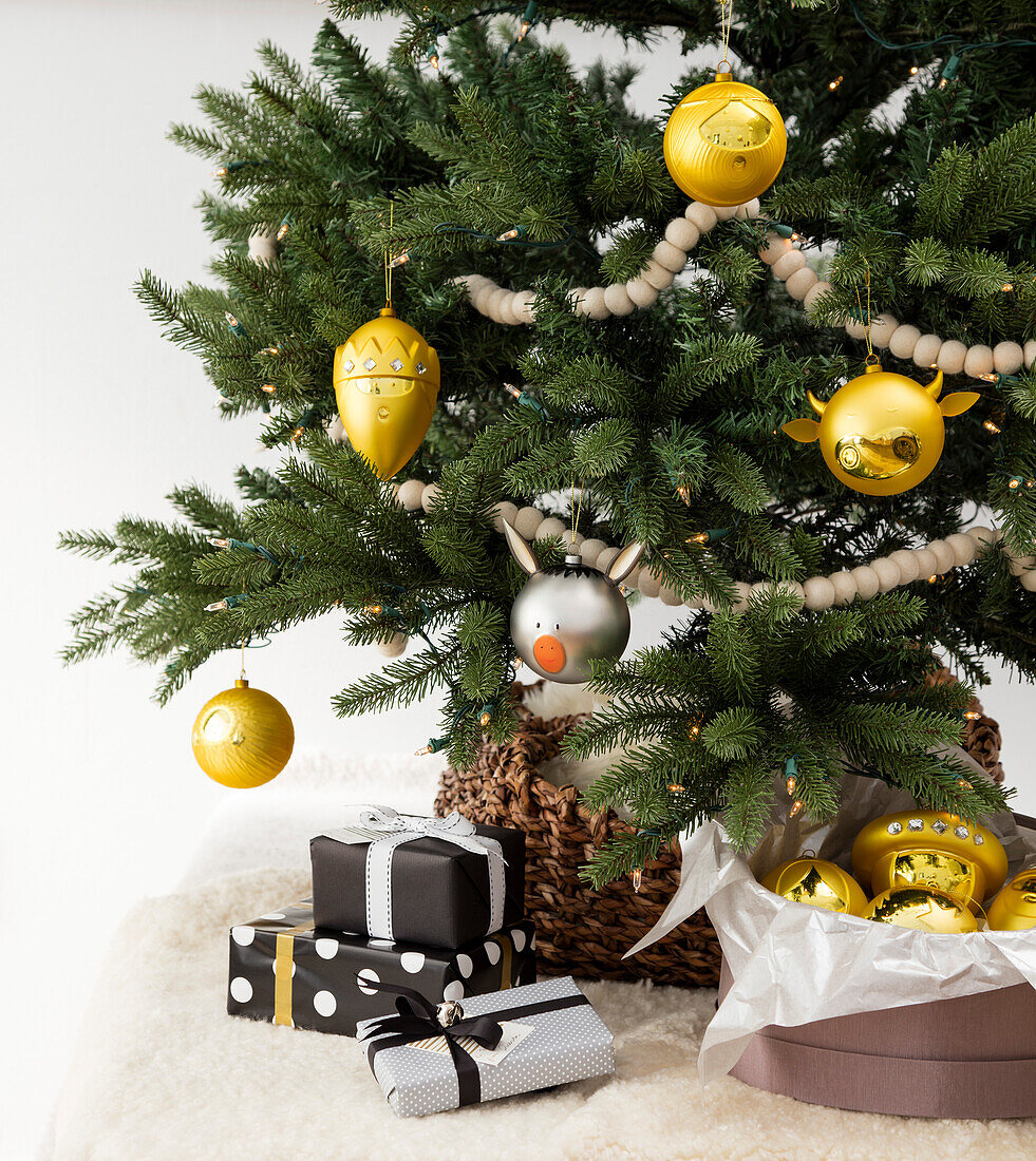 Geschenke unter dem mit gelben Ornamenten und einem silbernen Schwein geschmückten Weihnachtsbaum