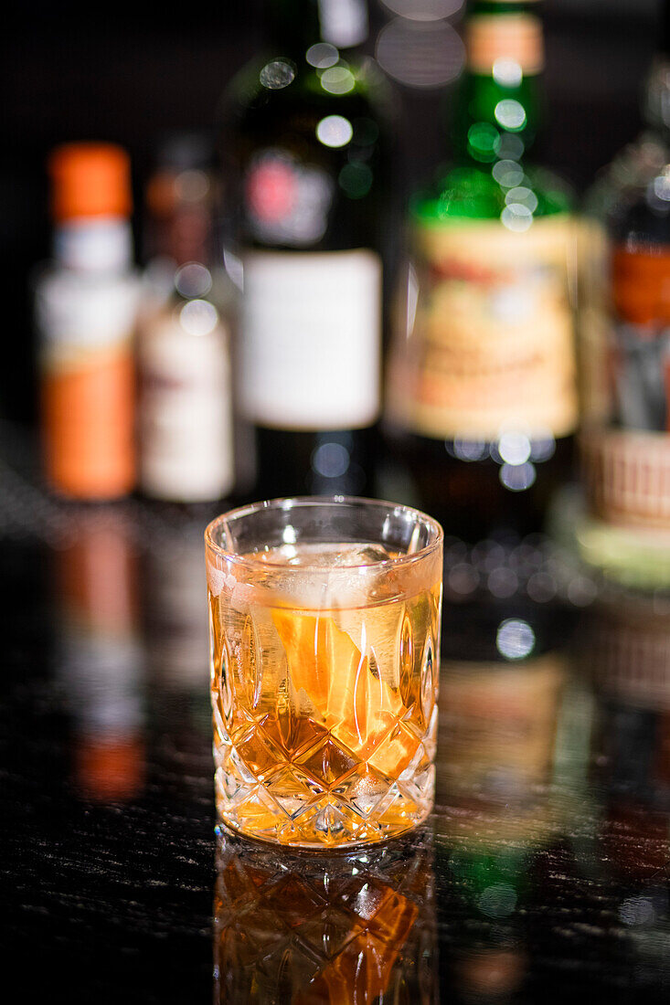 Alcohol cocktail with ice, liquor bottles in background