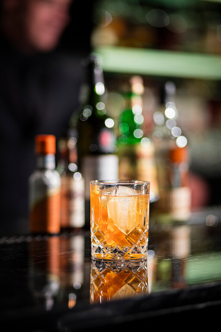 Alcohol cocktail with ice, liquor bottles in background