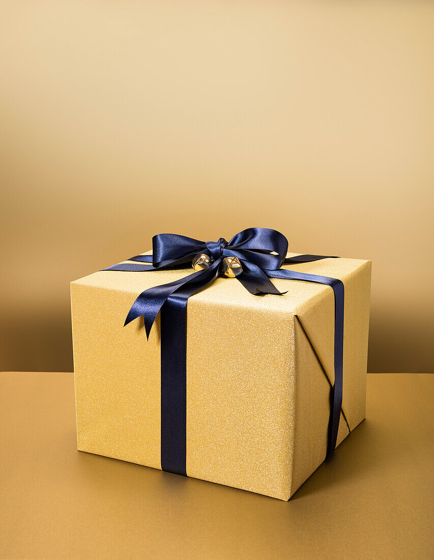 Eingepacktes Geschenk mit goldenem Geschenkpapier und schwarzer Schleife vor goldenem Hintergrund