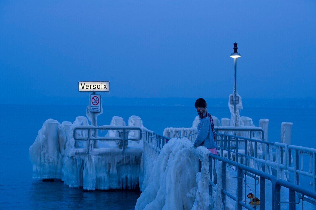 Schweiz, Kanton Waadt, Versoix, die Ufer des Genfer Sees sind bei sehr kaltem Wetter mit Eis bedeckt, eine Schaufensterpuppe auf dem mit Eis bedeckten Steg in der Abenddämmerung