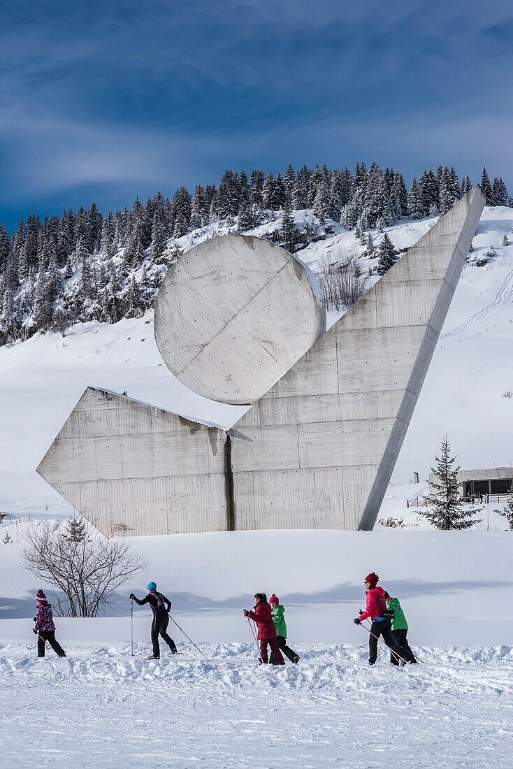 Frankreich, Haute Savoie, Bornes-Massiv, Plateau des Glieres, Kindergruppe auf der Langlaufloipe und das Nationaldenkmal des Widerstands von Emile Gilioli