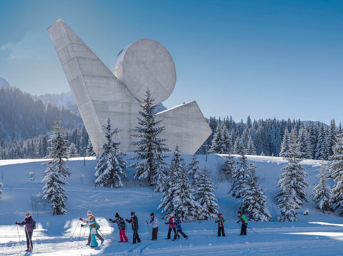 Frankreich, Haute Savoie, Bornes-Massiv, Plateau des Glieres, Panoramablick mit Kinderskatinggruppe auf Langlaufloipen und dem Nationaldenkmal des Widerstands von Emile Gilioli