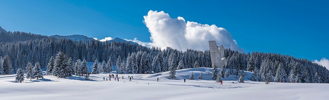 Frankreich, Haute Savoie, Bornes-Massiv, Plateau des Glieres, Panoramablick mit Kinderskatinggruppe auf Langlaufloipen und dem Nationaldenkmal des Widerstands von Emile Gilioli