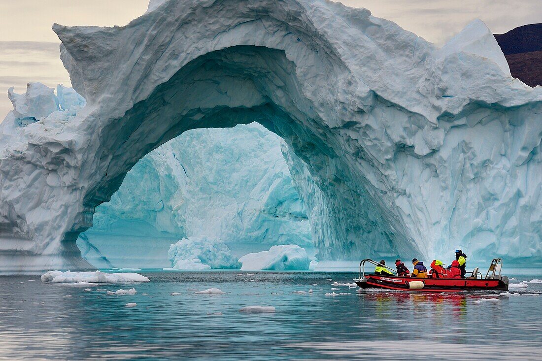 Grönland, Nordwestküste, Inglefield Fjord in Richtung Qaanaaq, Eisberg, der einen Bogen bildet, und ein Erkundungszodiac des Hurtigruten-Kreuzfahrtschiffs MS Fram