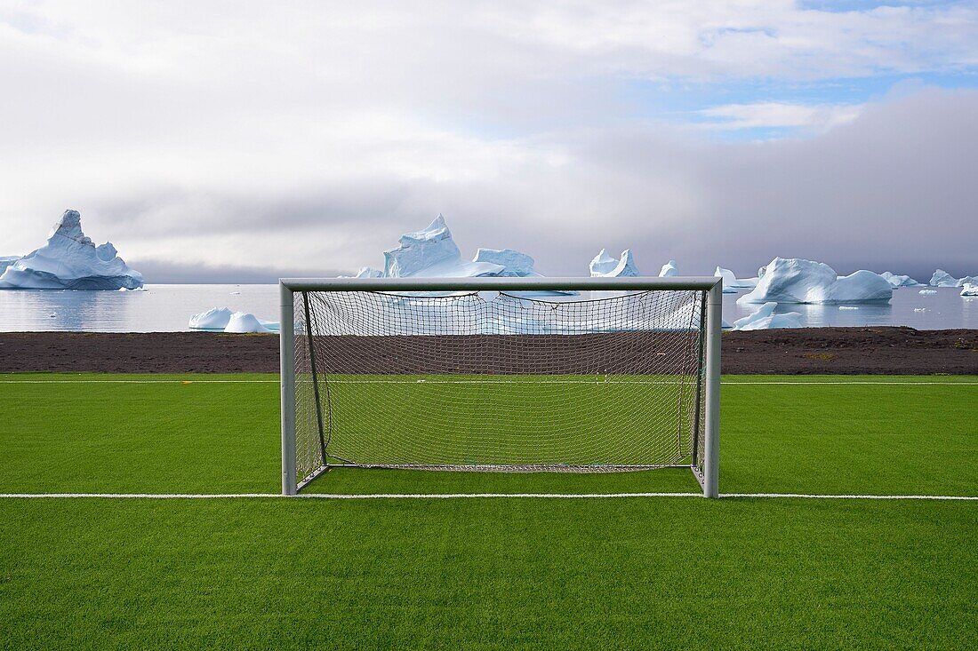 Greenland, west coast, Disko Island, Qeqertarsuaq, soccer field covered with synthetic grass and icebergs in the background