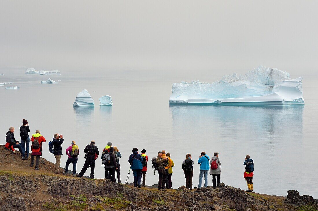 Grönland, Westküste, Disko Insel, Qeqertarsuaq, Wanderer an der Küste und Eisberge im Nebel im Hintergrund