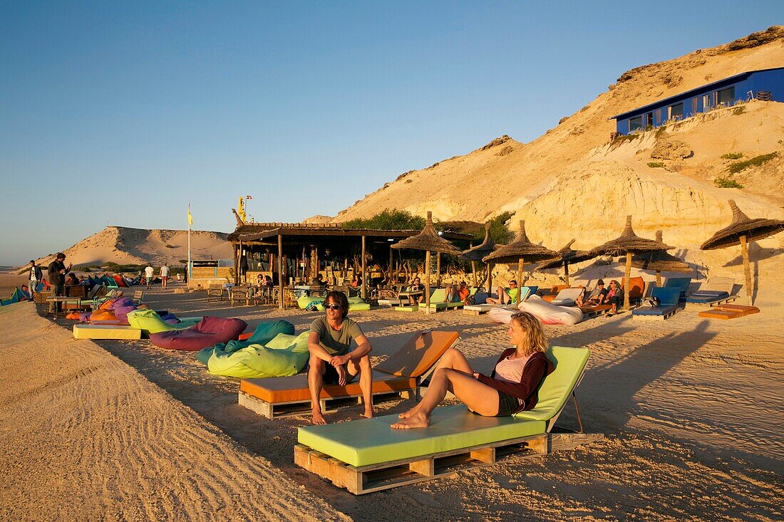 Marokko, Westsahara, Dakhla, Kitesurfer auf Liegestühlen vor der Kitecamp-Bar Dakhla Attitude bei Sonnenuntergang