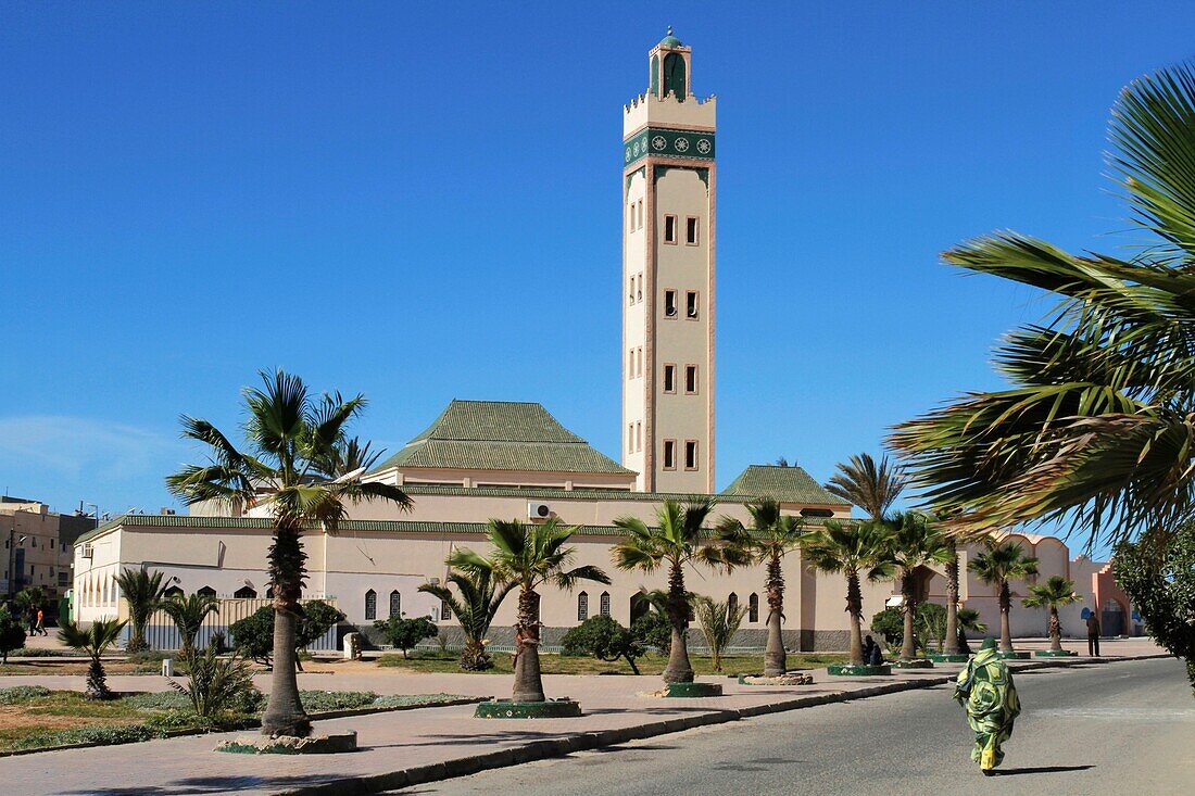 Morocco, Western Sahara, Dakhla, woman wearing traditional Saharawi clothing walking in front of Eddarham Mosque