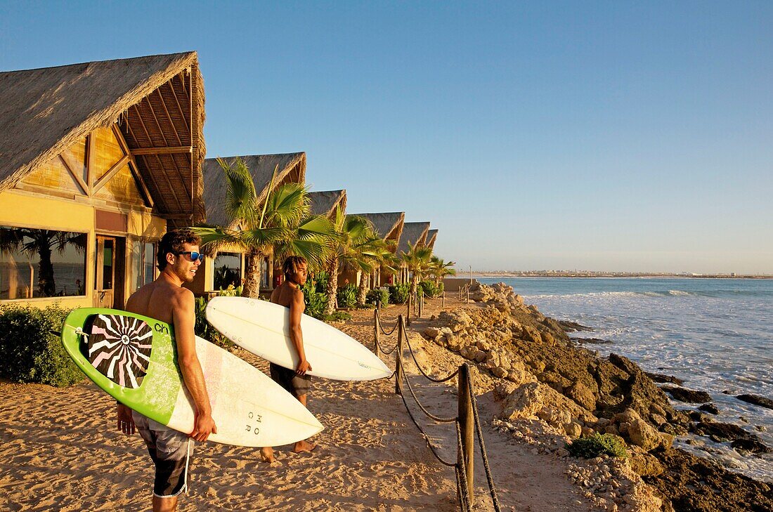 Marokko, Westsahara, Dakhla, marokkanische Surfer mit ihren Brettern vor dem Meer im West Point Hotel