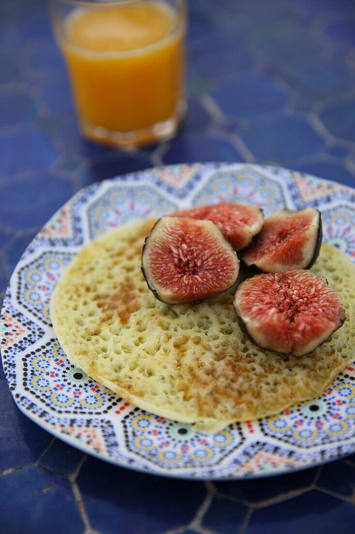 Marokko, Tanger Region Tetouan, Tanger, Pfannkuchen mit tausend Löchern und Feigen mit Honig auf einem Teller, begleitet von einem Glas Orangensaft auf einem zelligen Tisch