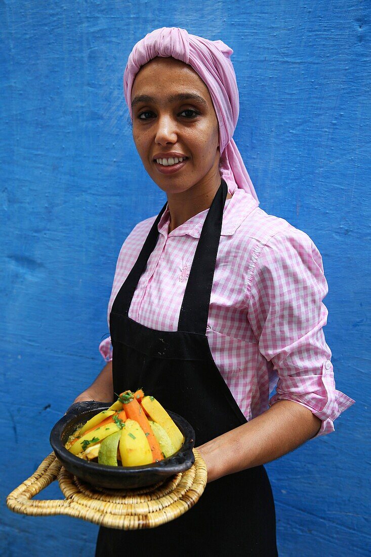 Marokko, Tanger Region Tetouan, Tanger, Marokkanische Frau mit einer Gemüsetagine in den Händen vor einer blauen Mauer Majorelle