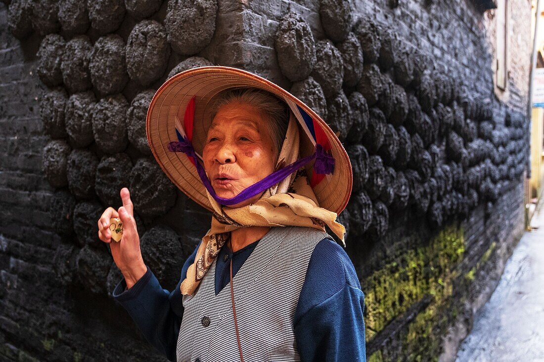 Vietnam, Bat Trang, near Hanoi, ceramist village, smiling woman front of clods of coal stuck on a wall of a traditional house