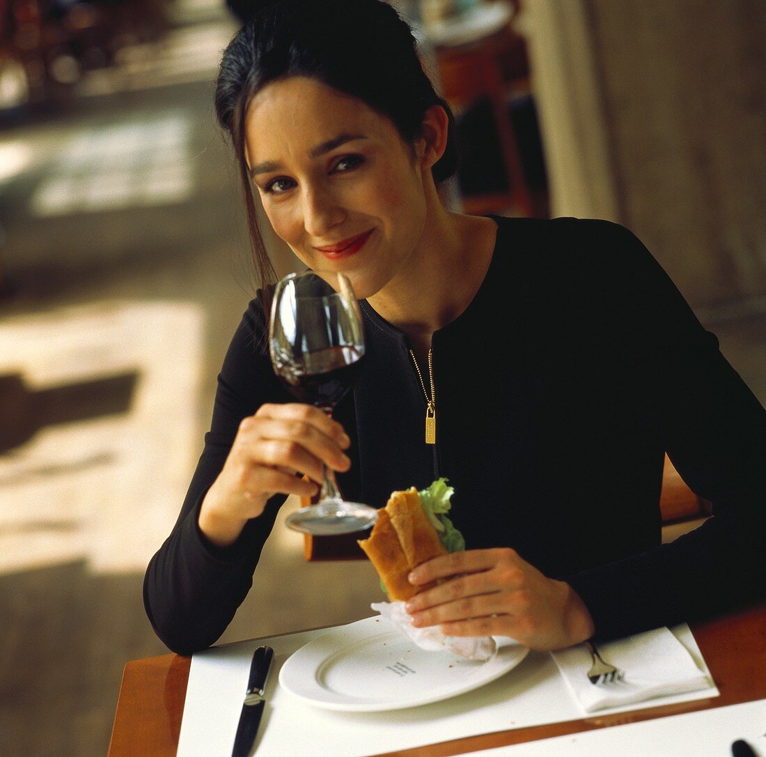 Frau isst ein Sandwich & trinkt ein Glas Rotwein im Bistro