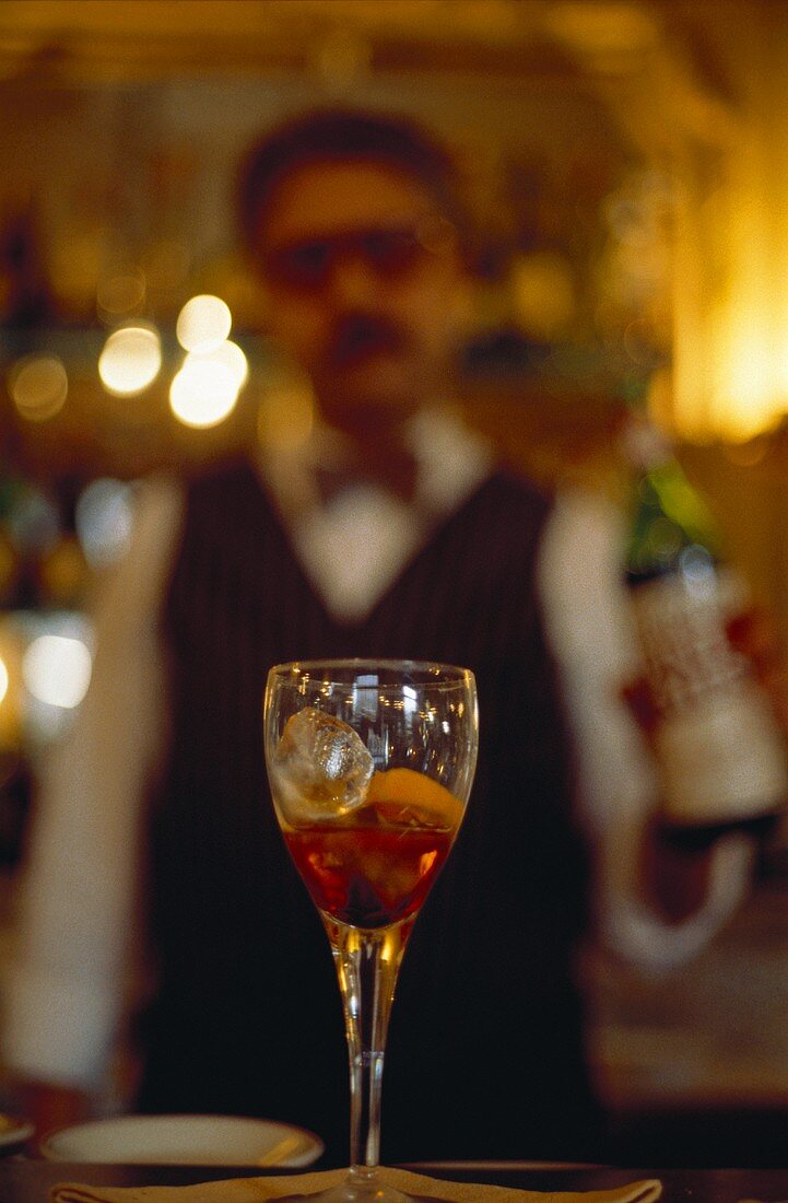 Cocktail in einer Bar, dahinter Kellner mit Flasche
