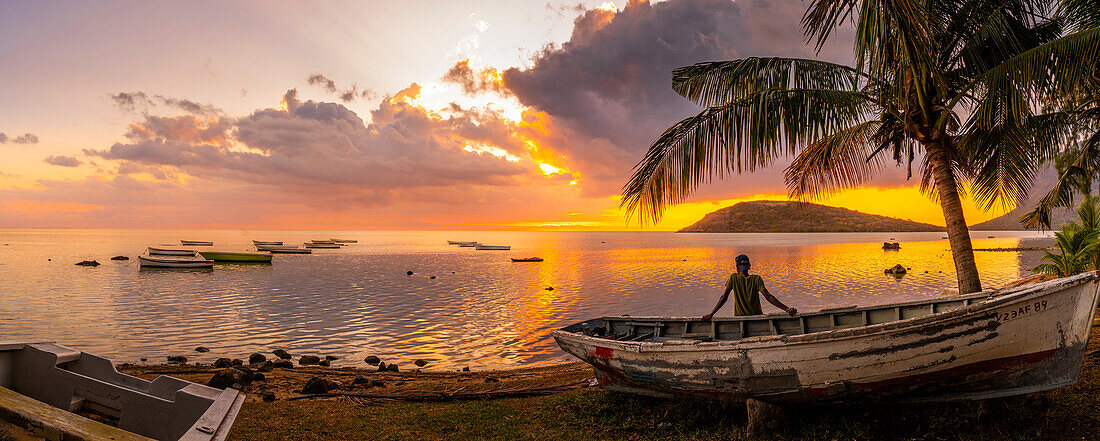 Blick auf einen Einheimischen, der auf einem Boot sitzt und Le Morne von Le Morne Brabant aus bei Sonnenuntergang betrachtet, Distrikt Savanne, Mauritius, Indischer Ozean, Afrika