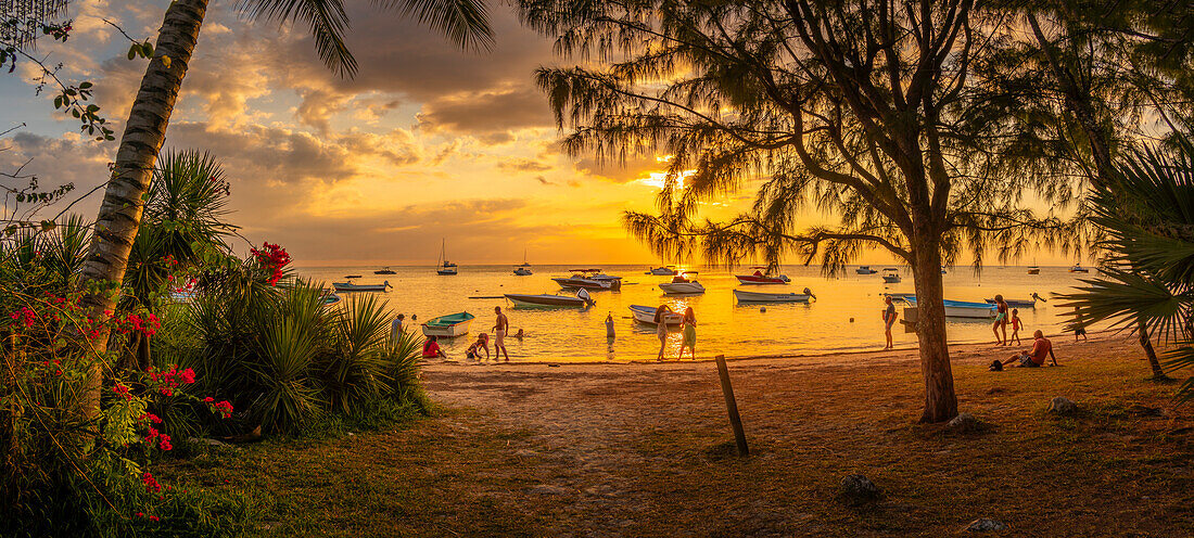 Blick auf Boote und Menschen am öffentlichen Strand von Mon Choisy bei Sonnenuntergang, Mauritius, Indischer Ozean, Afrika