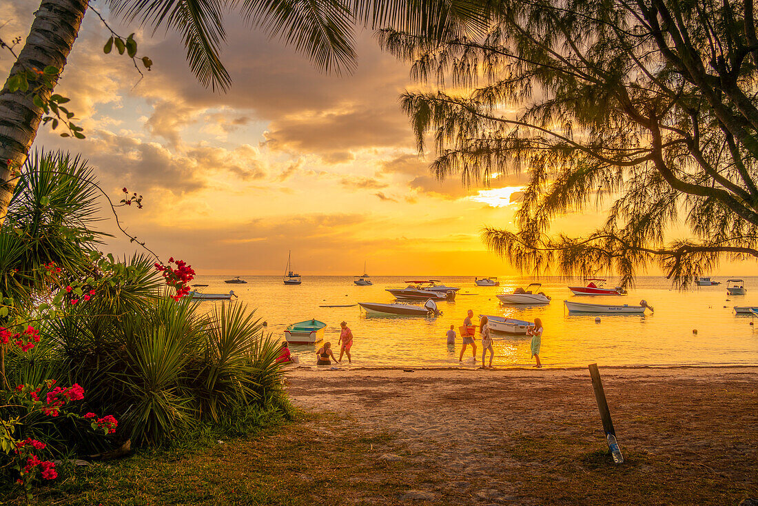 Blick auf Boote und Menschen am öffentlichen Strand von Mon Choisy bei Sonnenuntergang, Mauritius, Indischer Ozean, Afrika