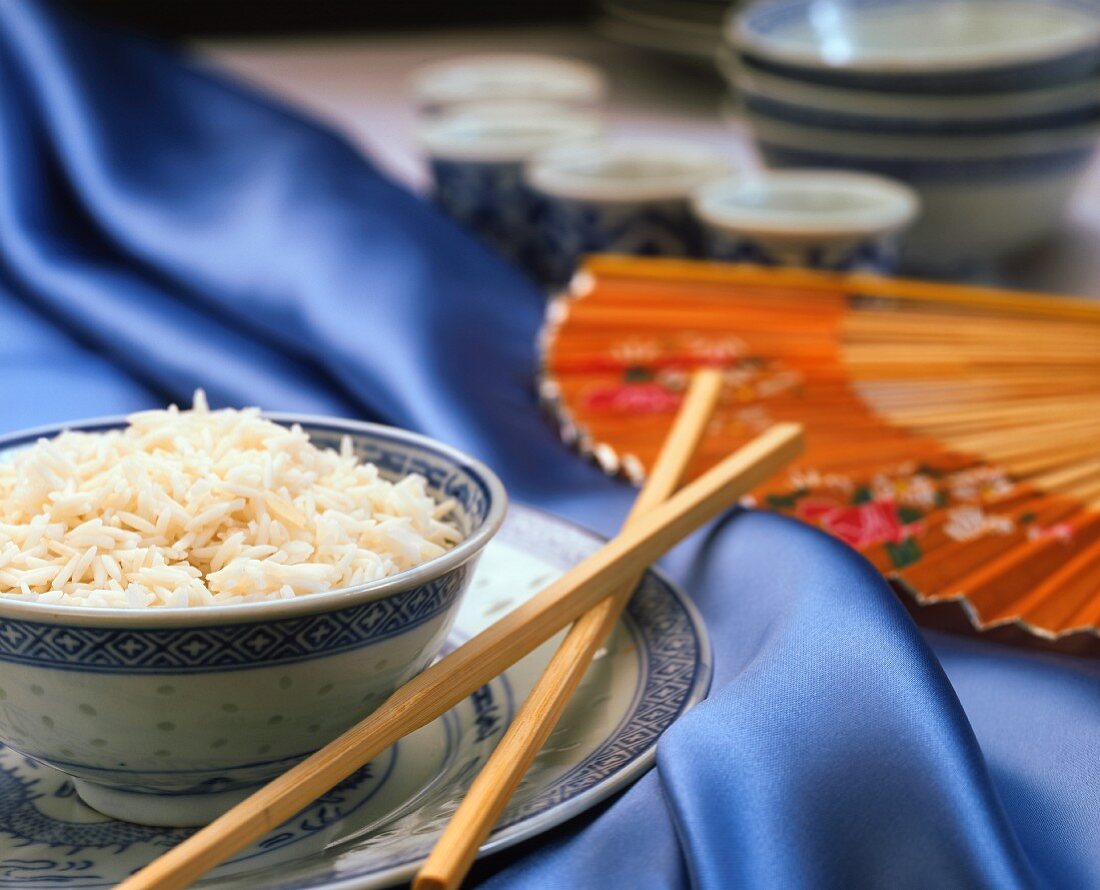 Reis in asiatischem Schälchen mit Stäbchen auf blauem Stoff