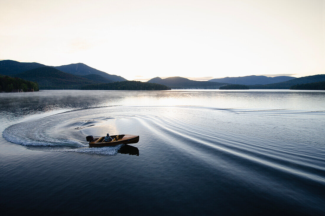 USA, New York, Lake Placid, Man in wooden boat on lake at sunrise