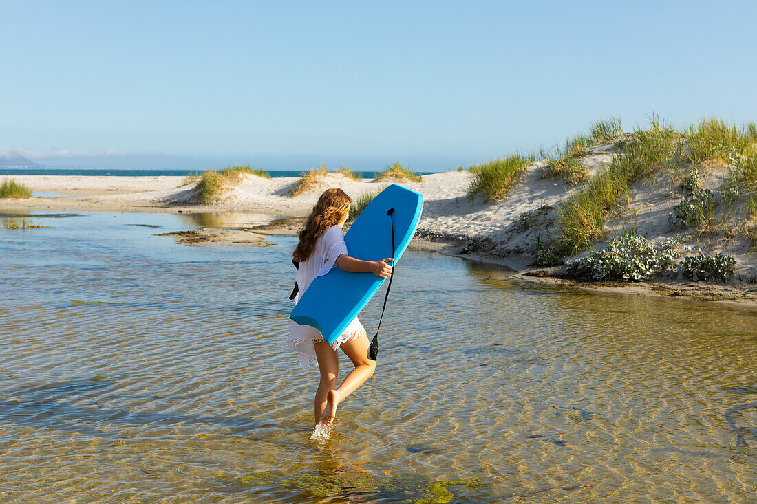 Südafrika, Hermanus, Teenager-Mädchen geht am Strand mit Bodyboard spazieren