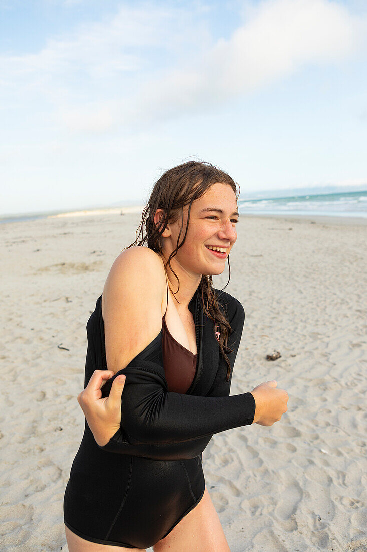 Südafrika, Hermanus, Teenager-Mädchen zieht Neoprenanzug am Strand an