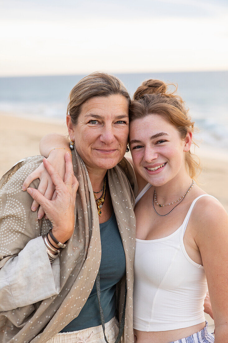 Porträt einer lächelnden Mutter und ihrer Tochter im Teenageralter am Strand