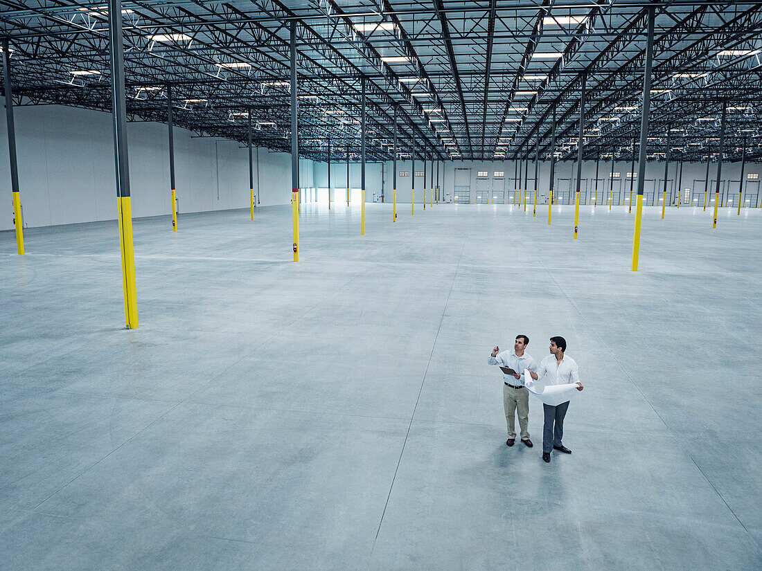 Architects with blueprint talking in empty warehouse