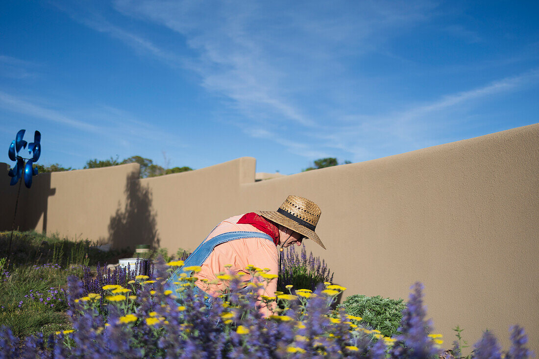 USA, New Mexico, Santa Fe, Woman in straw hat and denim overalls gardening