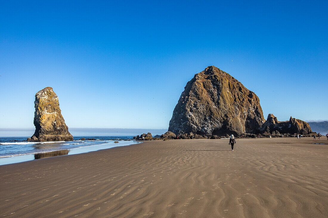 USA, Oregon, Rear view of woman walking near Haystack Rock at Cannon Beach