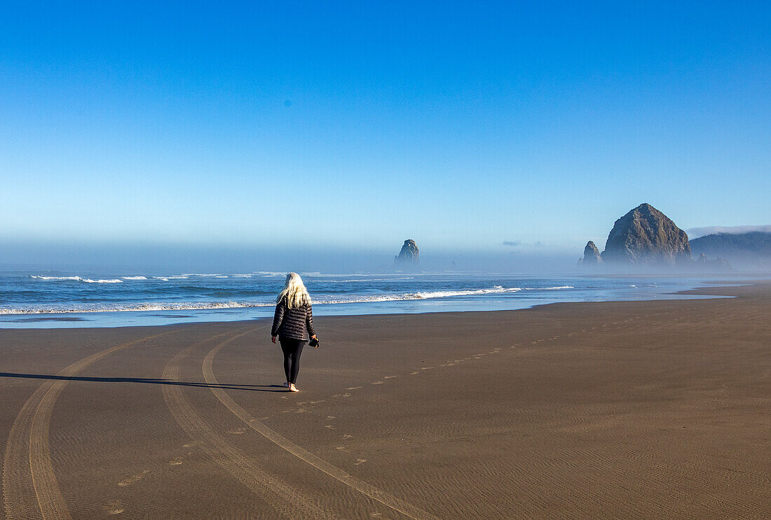 USA, Oregon, Rear view of woman walking near Haystack Rock at Cannon Beach in morning mist