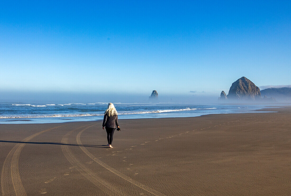 USA, Oregon, Rückansicht einer Frau bei einem Spaziergang in der Nähe des Haystack Rock in Cannon Beach im Morgennebel