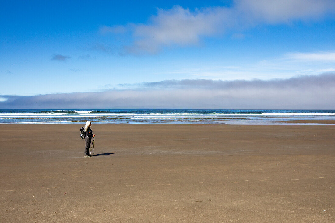 Woman standing on sandy beach and looking at view 