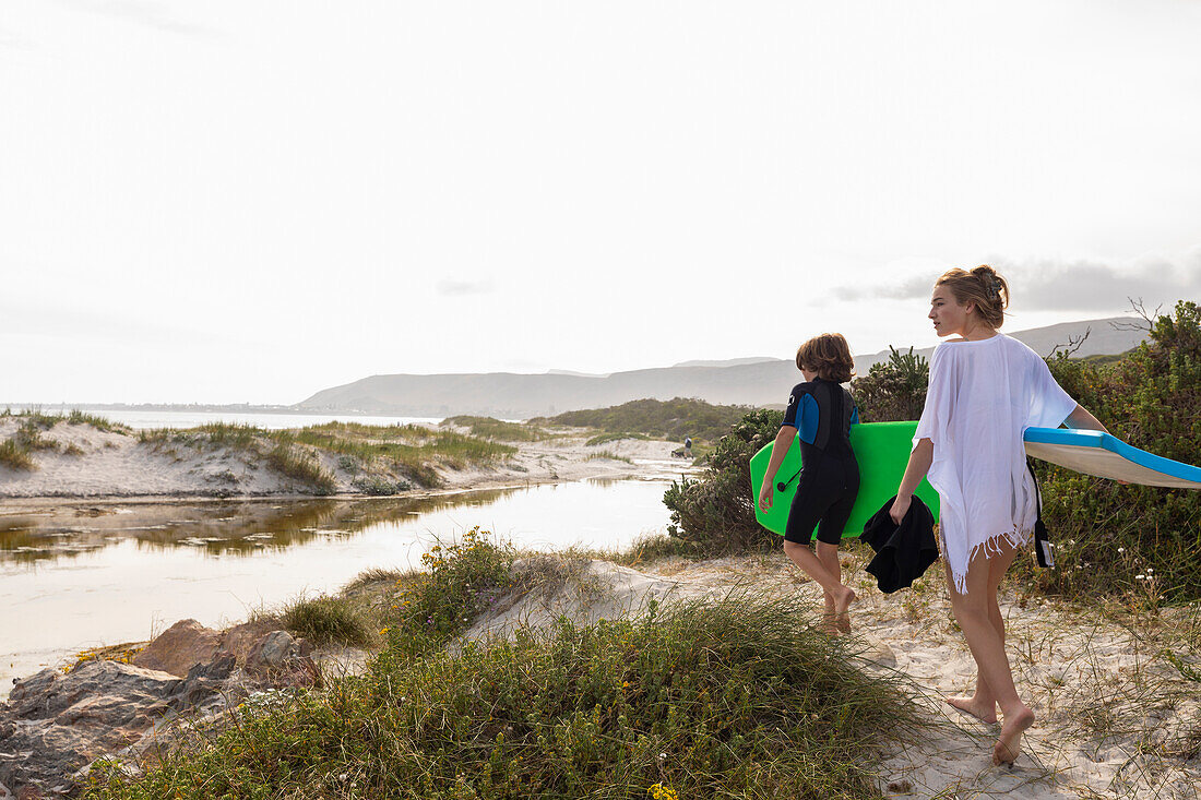 South Africa, Hermanus, Brother and sister walking on beach with body boards