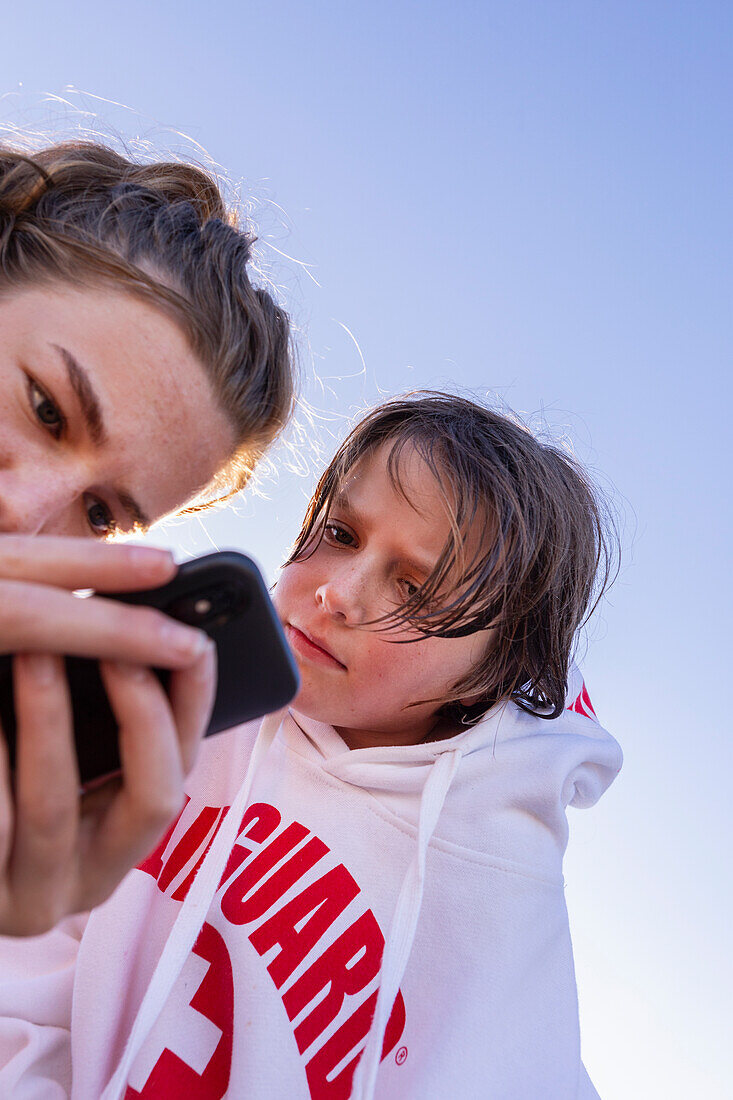 Bruder (10-11) und Schwester (16-17) schauen auf ihr Smartphone