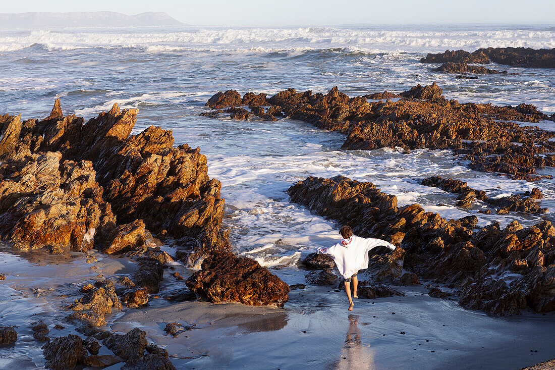 Südafrika, Hermanus, Junge (10-11) läuft zwischen Felsen am Kammabaai Beach