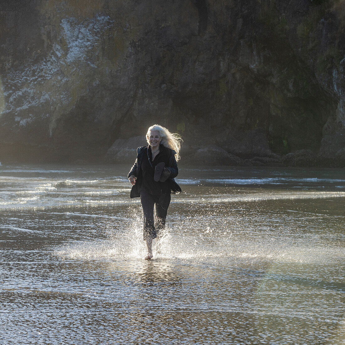 USA, Oregon, Newport, Frau läuft am Sandstrand und spritzt Wasser