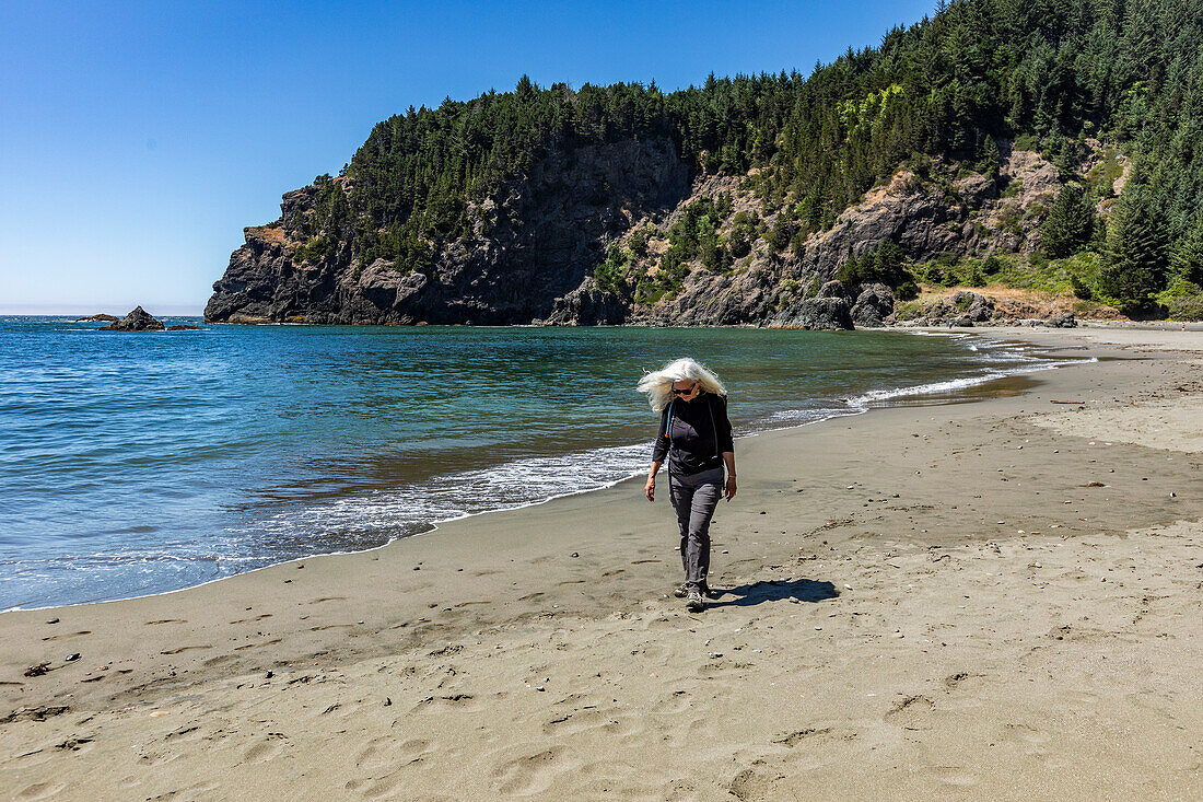 USA, Oregon, Brookings, Ältere Frau, die an einem sonnigen Tag am Strand spazieren geht
