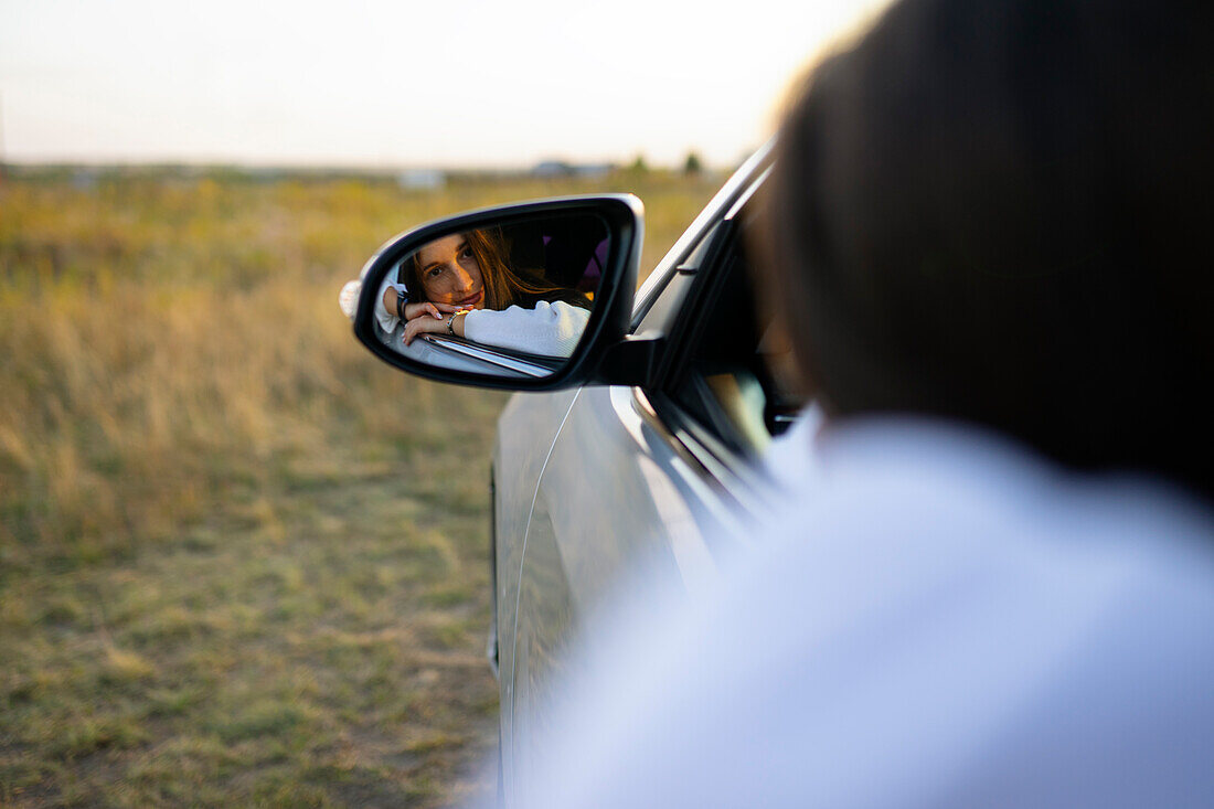 Reflection of young woman in car side view mirror 