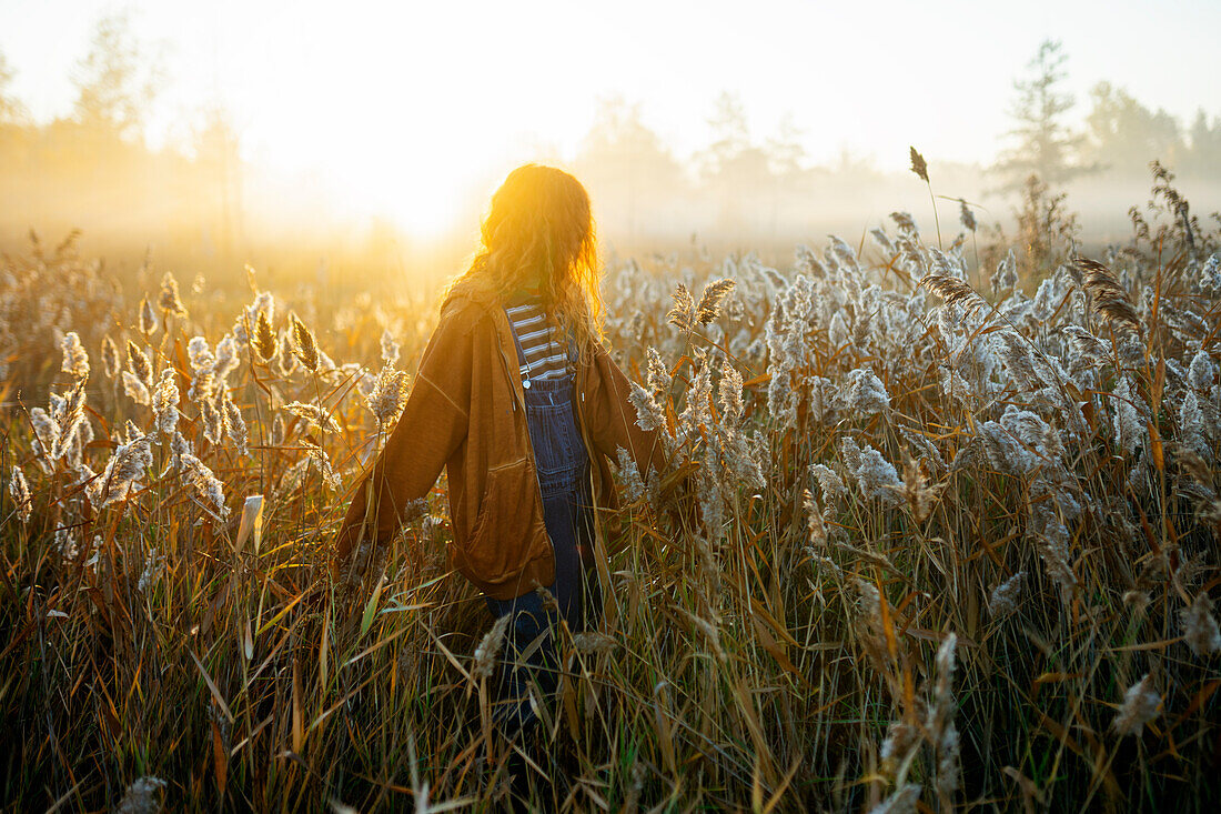 Junge Frau, die in der Morgendämmerung auf einem Feld spazieren geht