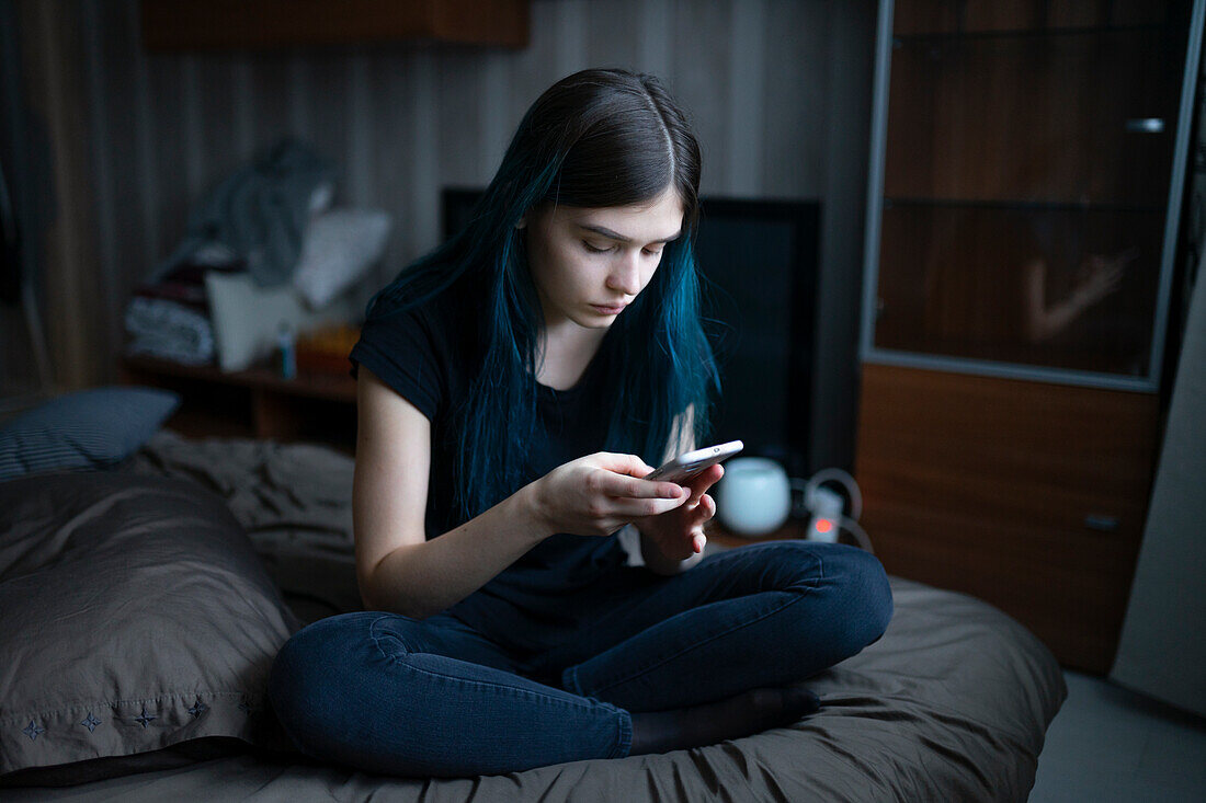 Ernste Frau, die auf dem Bett sitzend ein Smartphone benutzt