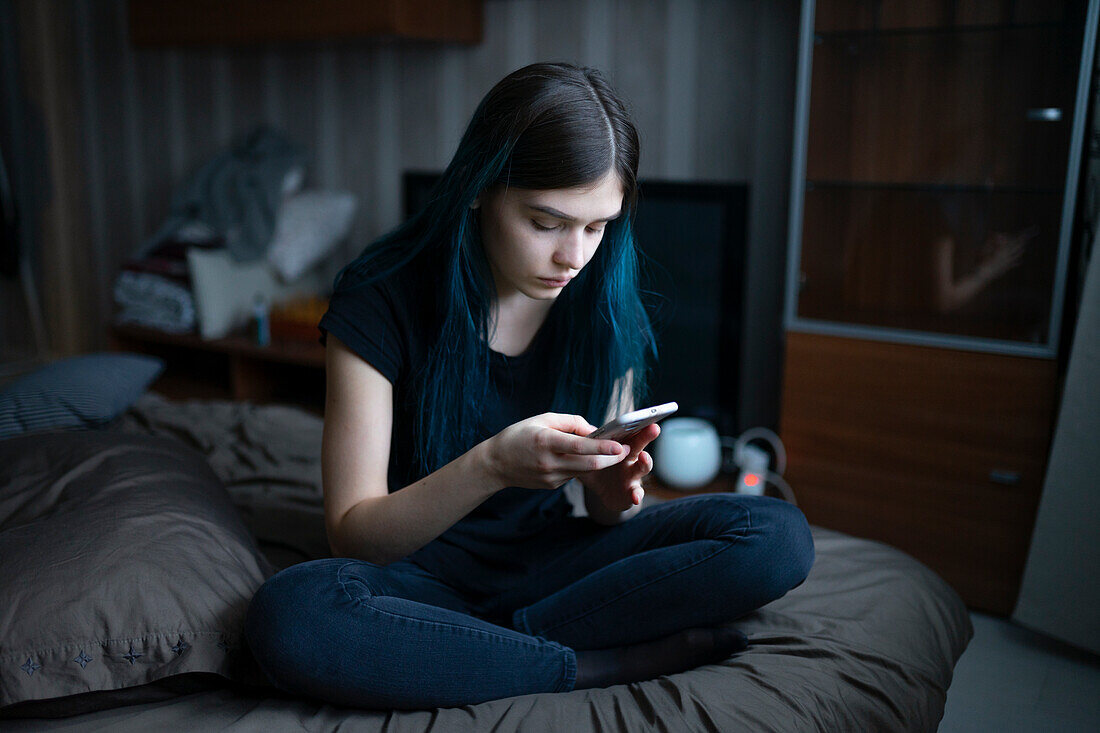 Serious woman using smart phone while sitting on bed