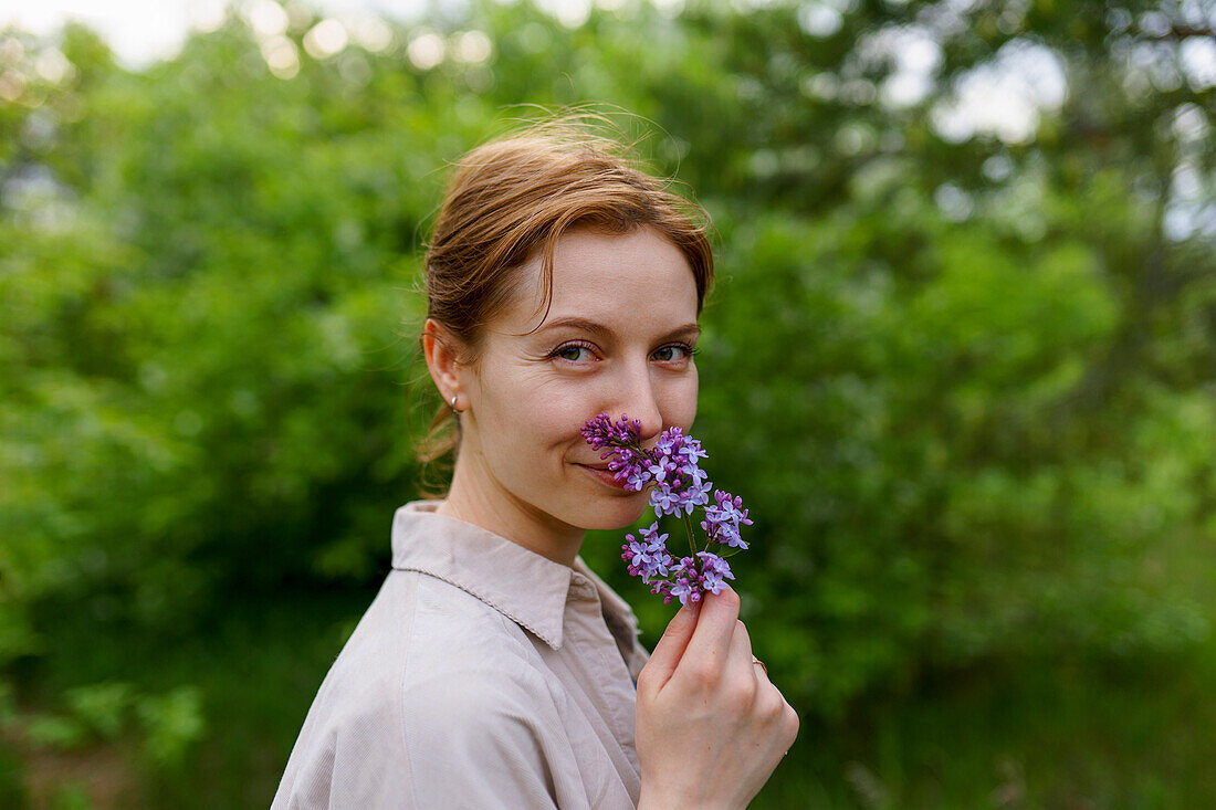 Porträt einer lächelnden Frau, die an einer Fliederblüte riecht