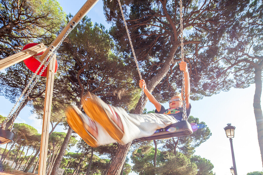 A child enjoys a swing set surrounded by pine trees