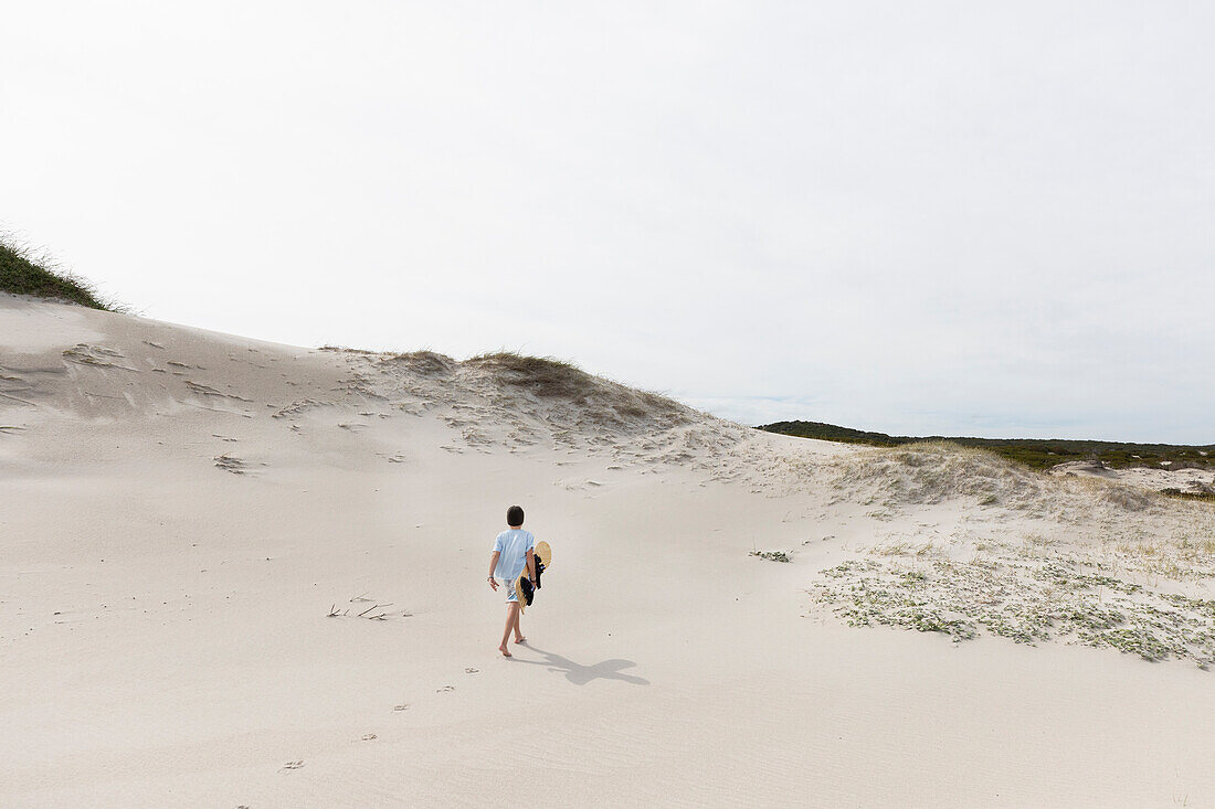 Junge (10-11) trägt Surfbrett im Walker Bay Naturreservat