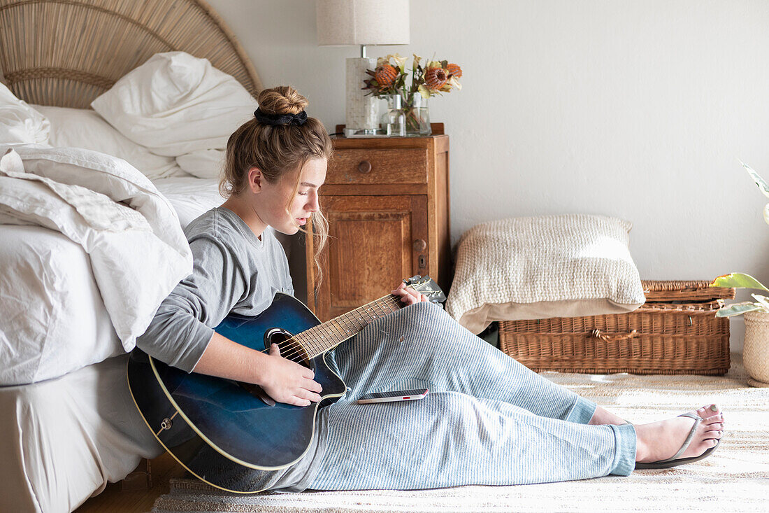 Teenage girl (16-17) playing guitar in bedroom